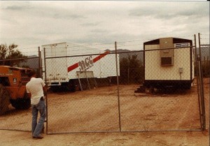 A man standing in front of a fence, possibly observing the work site.
