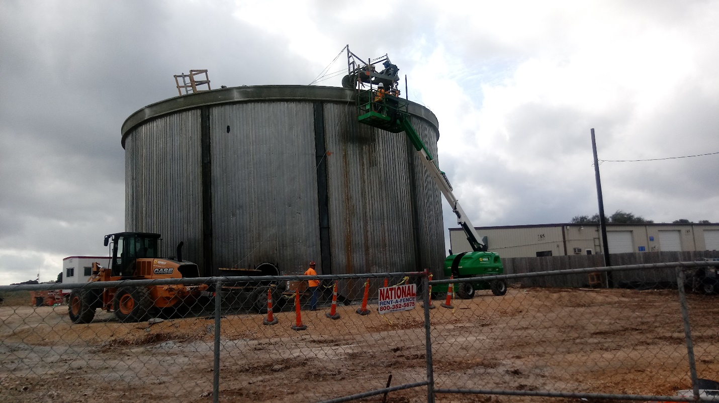 A worker is working on a large tank in a field.