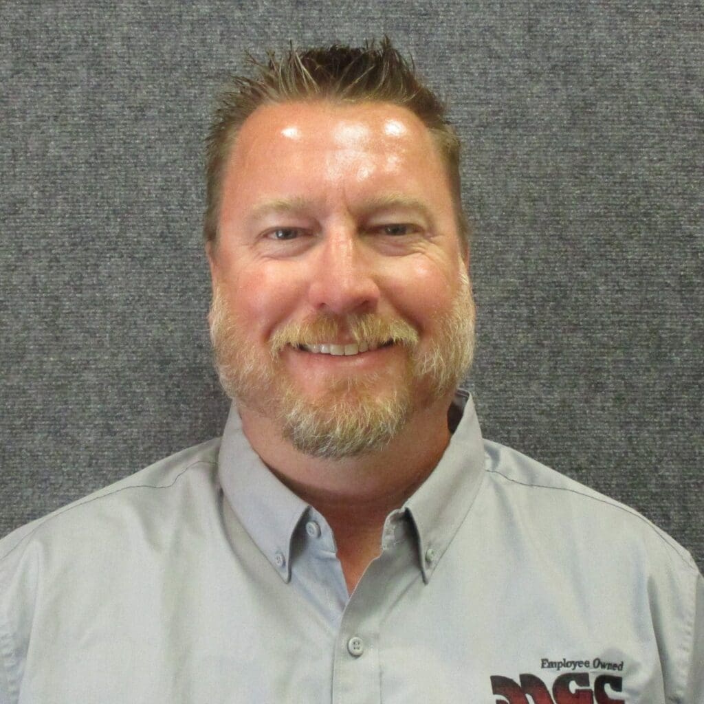 A man in a gray shirt smiling in front of a gray wall About MGC Contractors.