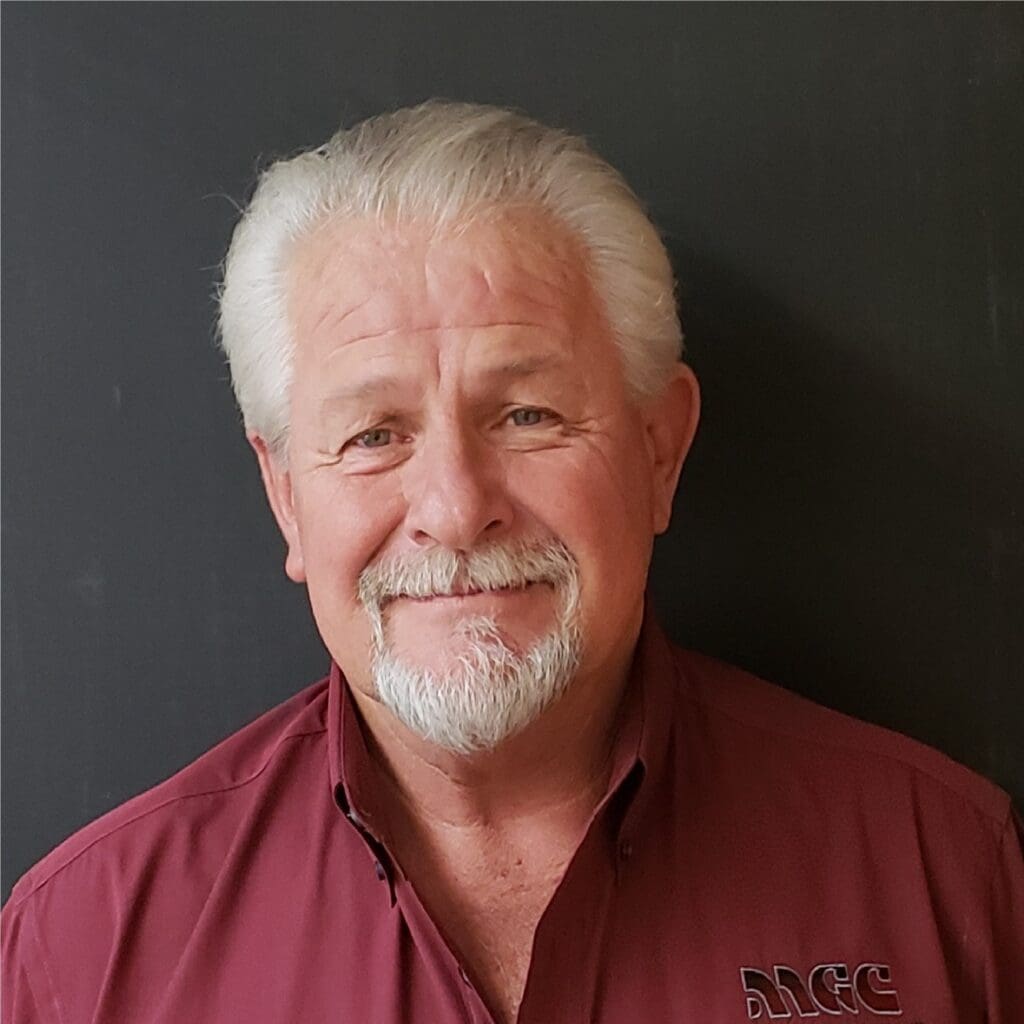 A man in a maroon shirt standing in front of a black wall, representing about mgc contractors.